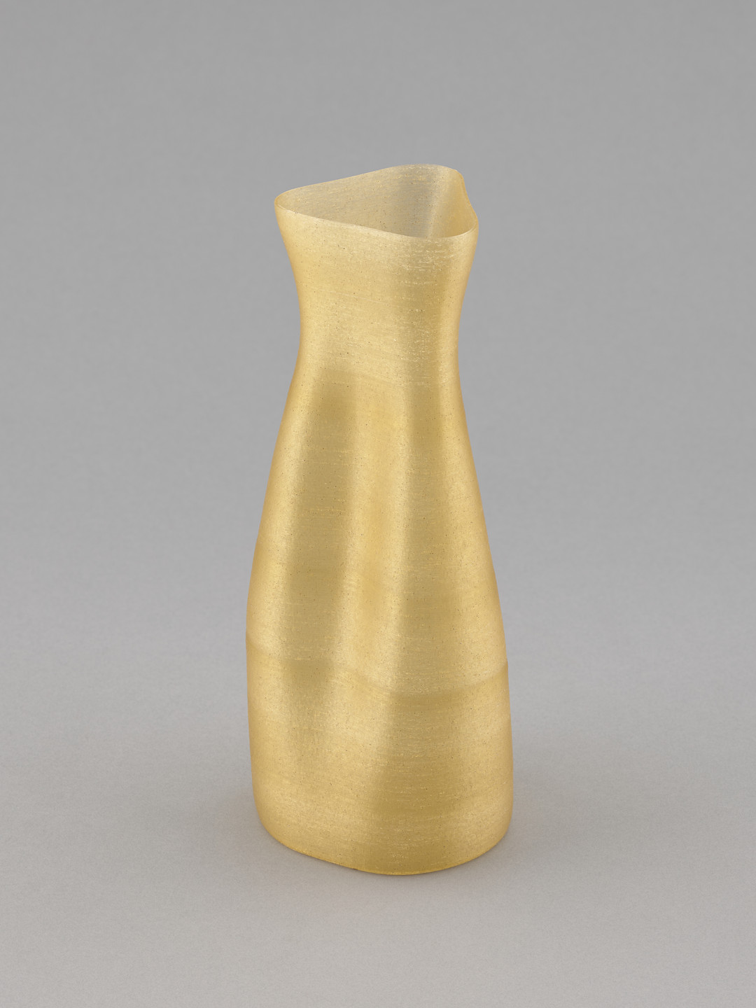 A gold, irregularly shaped vase with a narrow neck and wider, slightly uneven base stands against a plain gray background. The surface has a slightly metallic sheen. This is an AI generated description. To give feedback, email ai@moma.org.