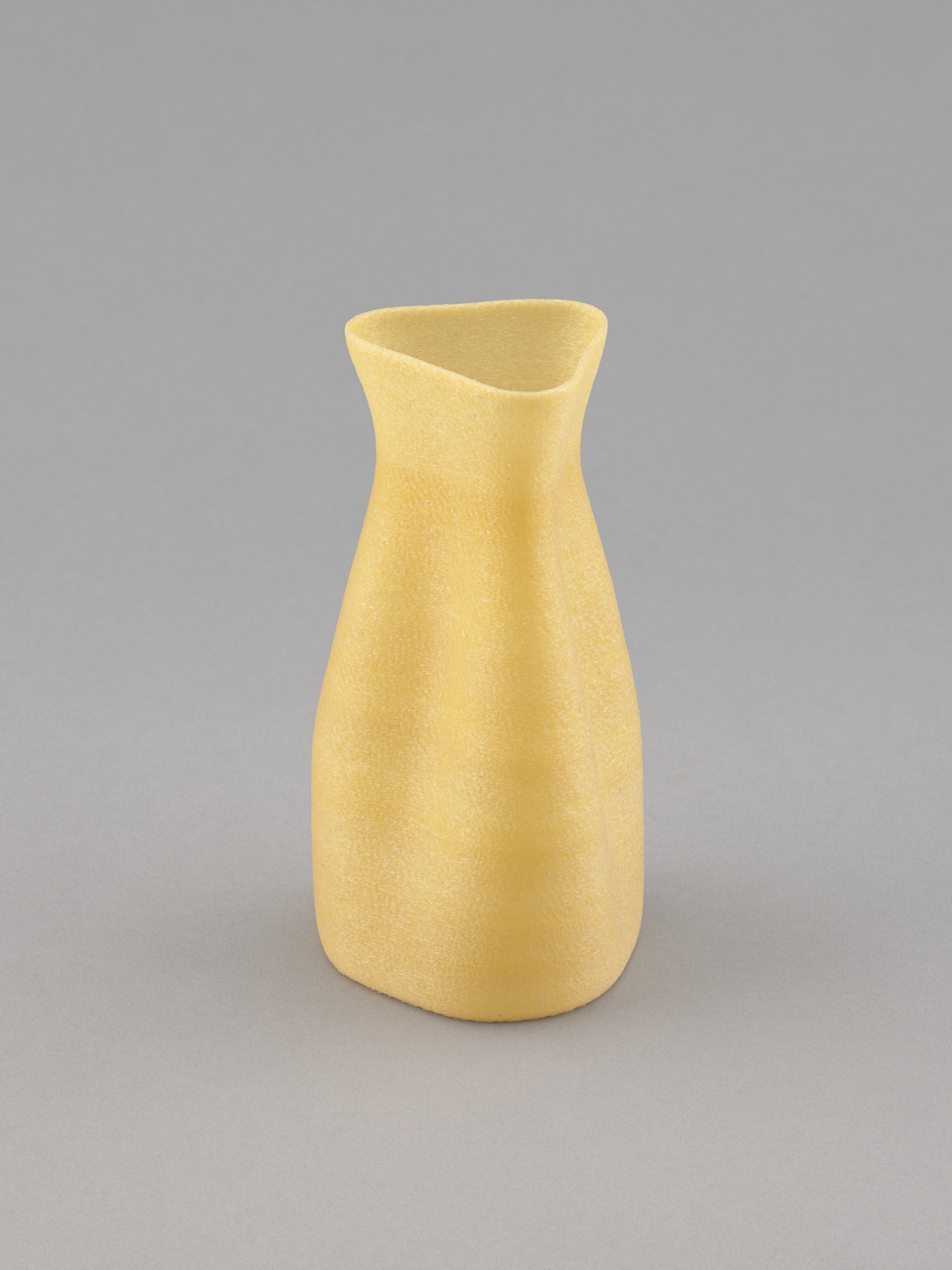 A beige, unevenly shaped, narrow-necked vase stands on a light gray surface. Its surface texture appears slightly rough. This is an AI generated description. To give feedback, email ai@moma.org.