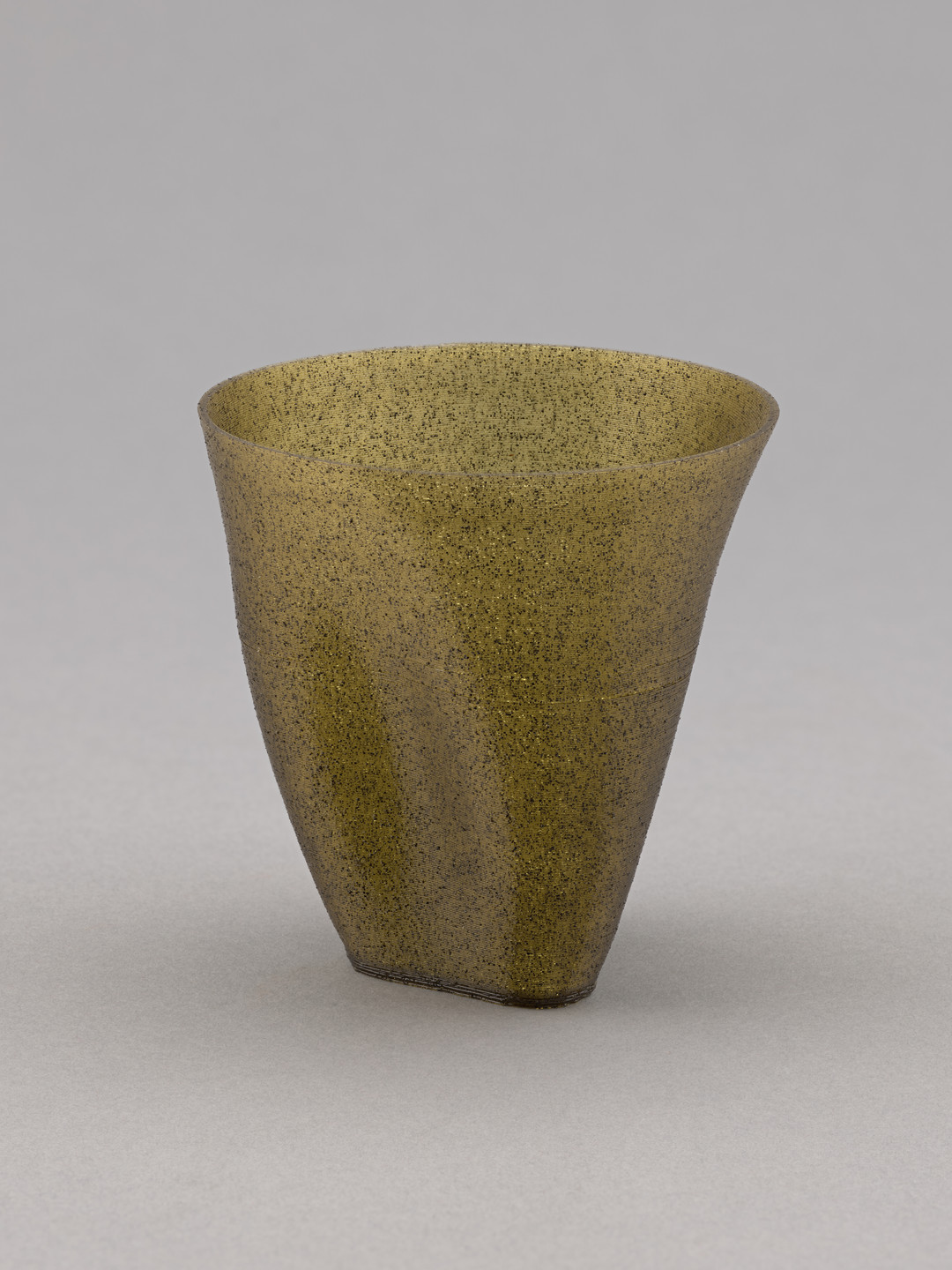 A textured, green-tinted vase with a wide, rounded opening tapers down to a smaller base against a plain gray background. The surface has a speckled pattern, giving it a rough appearance. This is an AI generated description. To give feedback, email ai@moma.org.