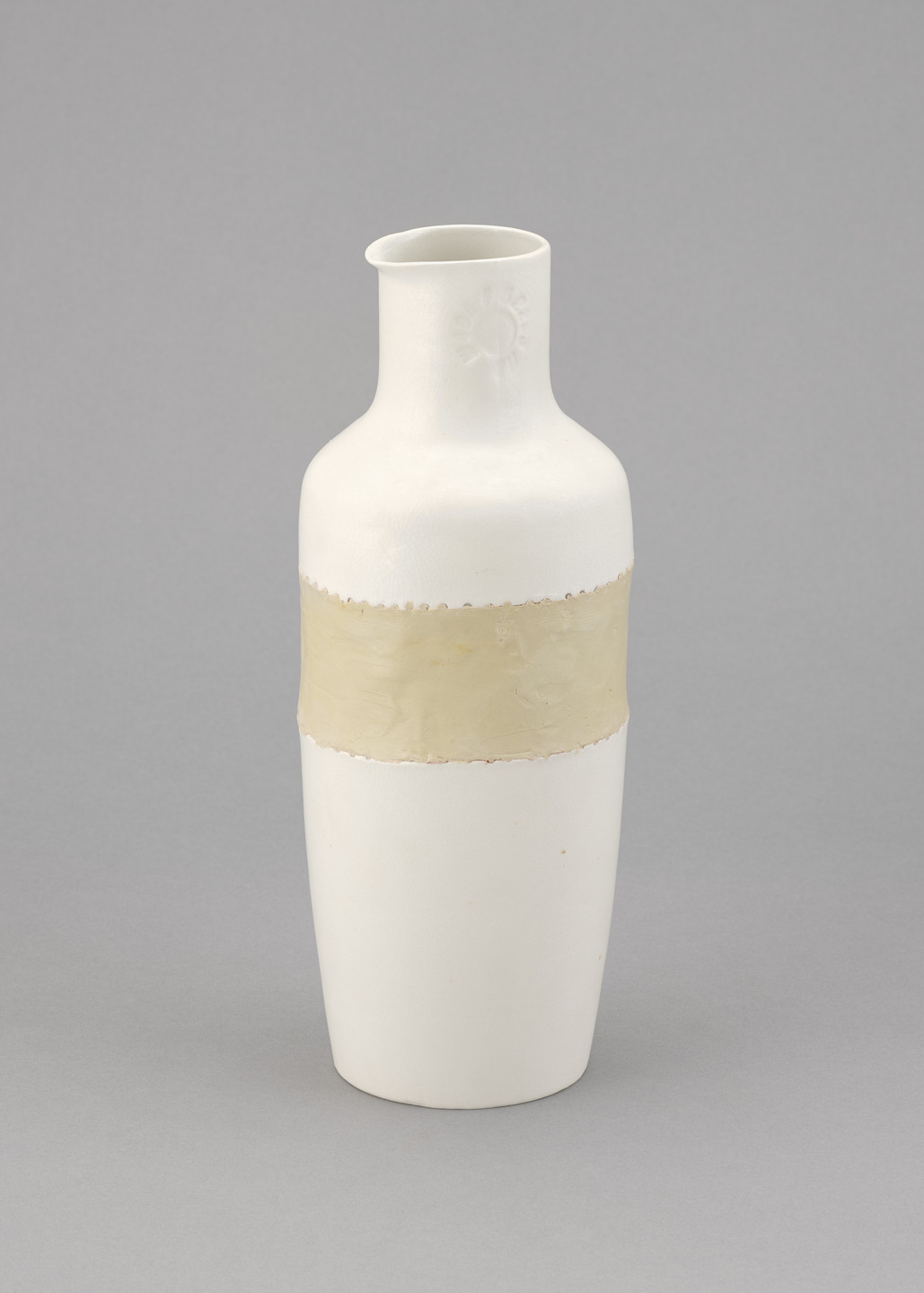 A white vase with a cylindrical shape has a beige horizontal band around its middle and a gray floral imprint near the neck. The vase is displayed against a light gray background. This is an AI generated description. To give feedback, email ai@moma.org.