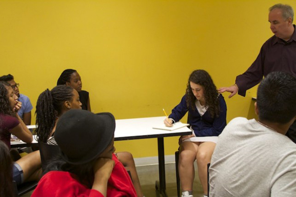 A participant draws a self-portrait while John Cerbone looks on