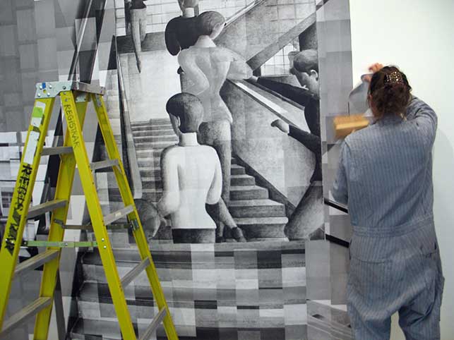 Katharina Gaenssler at work, October 28, 2015. Each sheet of paper is covered in paste, and then placed on the wall and re-coated with a wallpaper paste brush. Photo: Kristen Gaylord